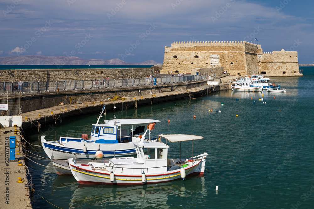 Fishing Boats under the walls of Koules Fortress in Heraklion. Fortress on the sea, tourist attraction of the city of Heraklion. Historic building in Crete, Greece.