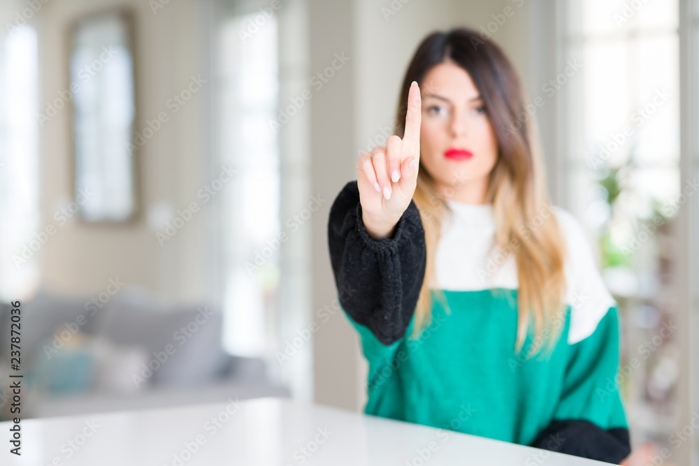 Young beautiful woman wearing winter sweater at home Pointing with finger up and angry expression Young beautiful woman wearing winter sweater at home Pointing with finger up and angry expression