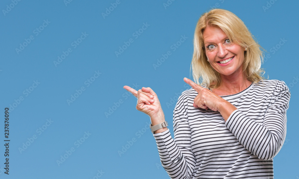 Middle age blonde woman over isolated background smiling and looking at the camera pointing with two hands and fingers to the side. Middle age blonde woman over isolated background smiling and looking at the camera pointing with two hands and fingers to the side.