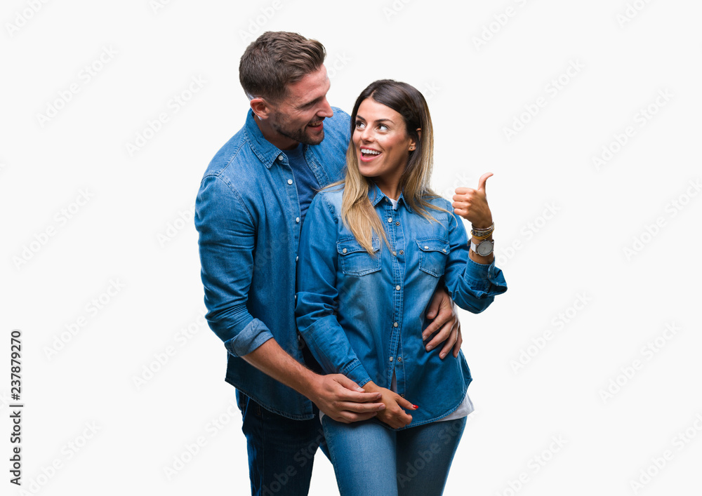 Young couple in love over isolated background smiling with happy face looking and pointing to the side with thumb up. Young couple in love over isolated background smiling with happy face looking and pointing to the side with thumb up.