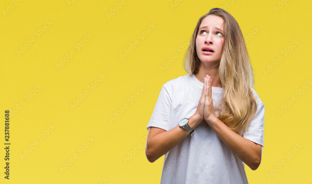 Young beautiful blonde woman wearing casual white t-shirt over isolated background begging and praying with hands together with hope expression on face very emotional and worried Young beautiful blonde woman wearing casual white t-shirt over isolated background begging and praying with hands together with hope expression on face very emotional and worried