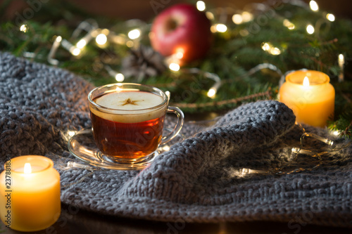 Hot mulled apple cider on woolen scarf and candle, wooden background