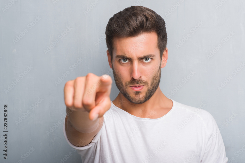 Handsome young man over grey grunge wall pointing with finger to the camera and to you, hand sign, positive and confident gesture from the front Handsome young man over grey grunge wall pointing with finger to the camera and to you, hand sign, positive and confident gesture from the front