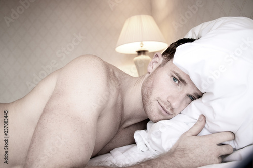 Handsome muscular naked men with blue eyes lying on hotel bed sheets looking at camera