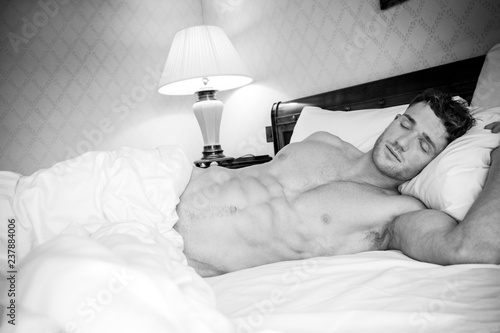 Handsome hunky muscular man with six pack abs sleeping in between white sheets in hotel bed photo