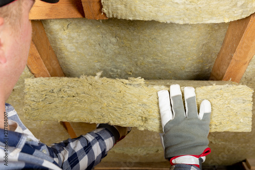 Man installing thermal roof insulation layer - using mineral wool panels. Attic renovation and insulation concept