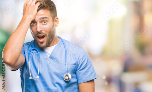 Young handsome doctor surgeon man over isolated background surprised with hand on head for mistake, remember error. Forgot, bad memory concept.