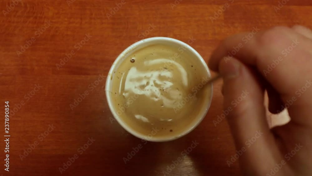 Cup of coffee on wooden table. Hand stirring coffee in a cup on wooden table Cup of coffee on wooden table. Hand stirring coffee in a cup on wooden table