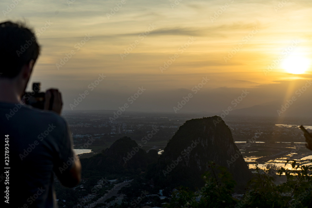 Tourist staying on the top of mountain and taking a photos of Marble mountains and beautiful Da Nang city view with jungle and sea in sunset,travelling concept