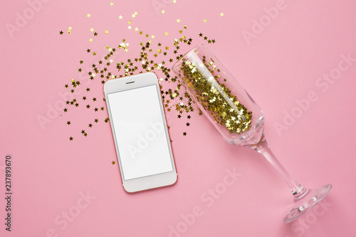 Mobile phone and champagne glasses with golden stars confetti on pink color paper background minimal style