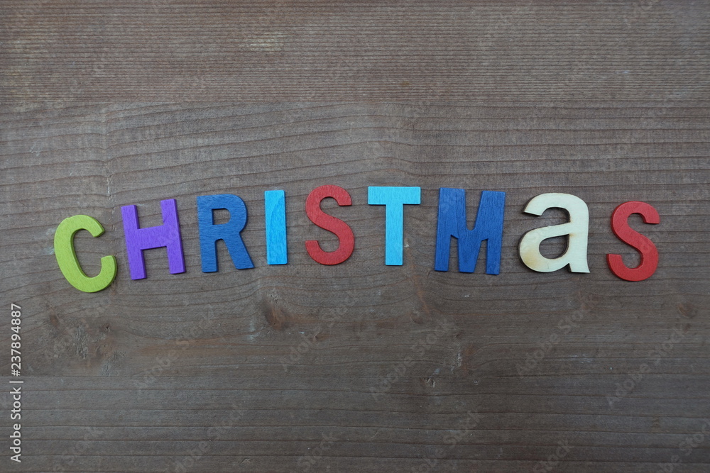 Fototapeta premium Christmas word with colored wooden letters over a brown board