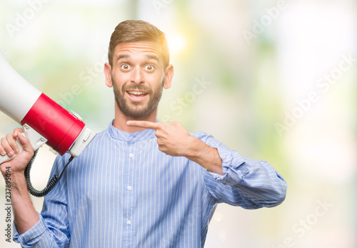 Young handsome man yelling through megaphone over isolated background very happy pointing with hand and finger
