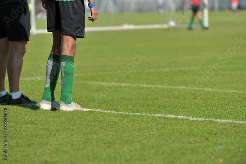 A substitution football player waiting on the side line with his coach while watching his teammate in a Boys' Under 18 years school soccer tournament.