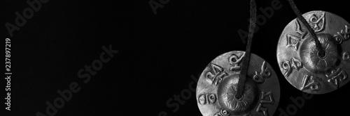 Tingsha Cymbals Tibetan Buddhist Lucky Symbol Embossed Meditation Yoga Bell Chimes on black contrasting background. Tibetan singing mantra bells. Header for a site about meditation. Black and white.