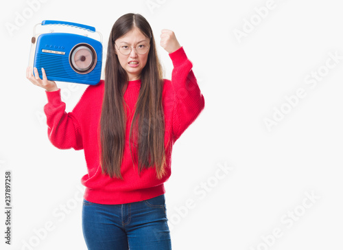 Young Chinese woman over isolated background holding vintage radio annoyed and frustrated shouting with anger, crazy and yelling with raised hand, anger concept