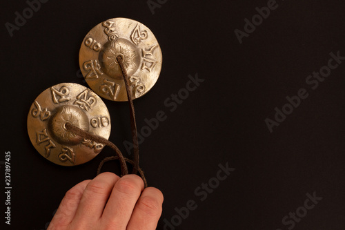 Bronze mystical Tibetan karatal meditation lies in the male hand on a contrasting black floor. Tibetan ringing plates for relaxation and recovery during meditation.