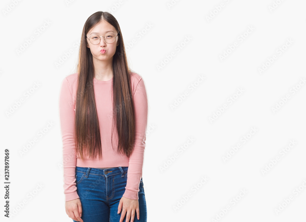 Young Chinese woman over isolated background wearing glasses puffing cheeks with funny face. Mouth inflated with air, crazy expression. Young Chinese woman over isolated background wearing glasses puffing cheeks with funny face. Mouth inflated with air, crazy expression.