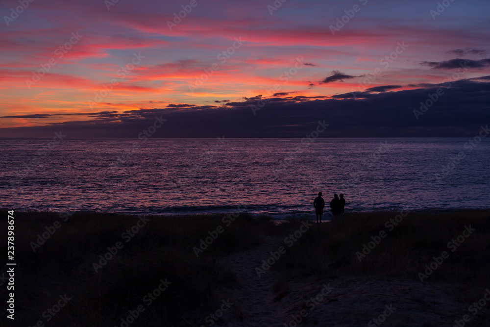 Silhouette of three people at beach sunset in Normandy, France