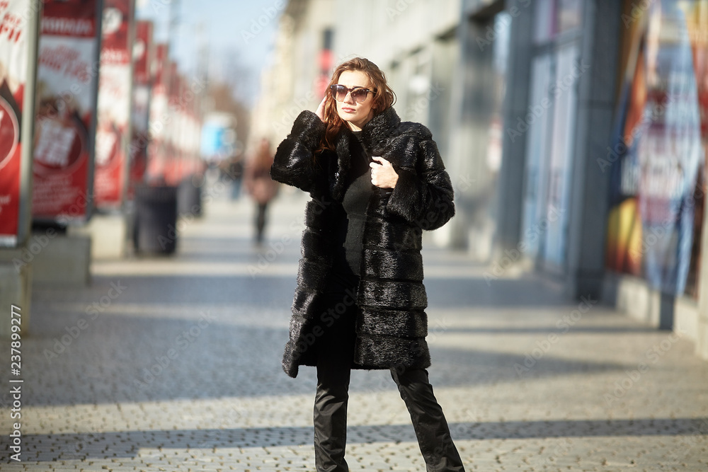 Fototapeta premium The girl walks through the city in a fur coat