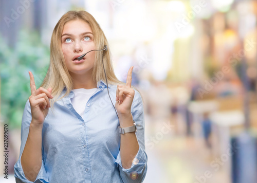 Young caucasian business woman wearing call center headset over isolated background amazed and surprised looking up and pointing with fingers and raised arms. © Krakenimages.com