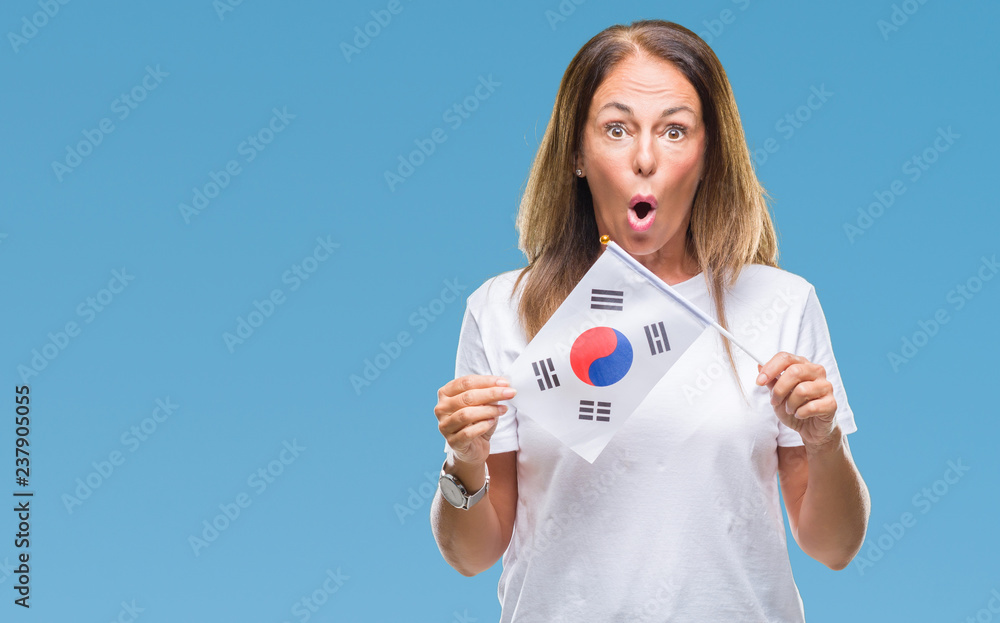 Middle age hispanic woman holding flag of South Korea over isolated background scared in shock with a surprise face, afraid and excited with fear expression Middle age hispanic woman holding flag of South Korea over isolated background scared in shock with a surprise face, afraid and excited with fear expression