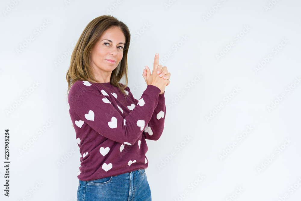 Beautiful middle age woman wearing heart sweater over isolated background Holding symbolic gun with hand gesture, playing killing shooting weapons, angry face Beautiful middle age woman wearing heart sweater over isolated background Holding symbolic gun with hand gesture, playing killing shooting weapons, angry face