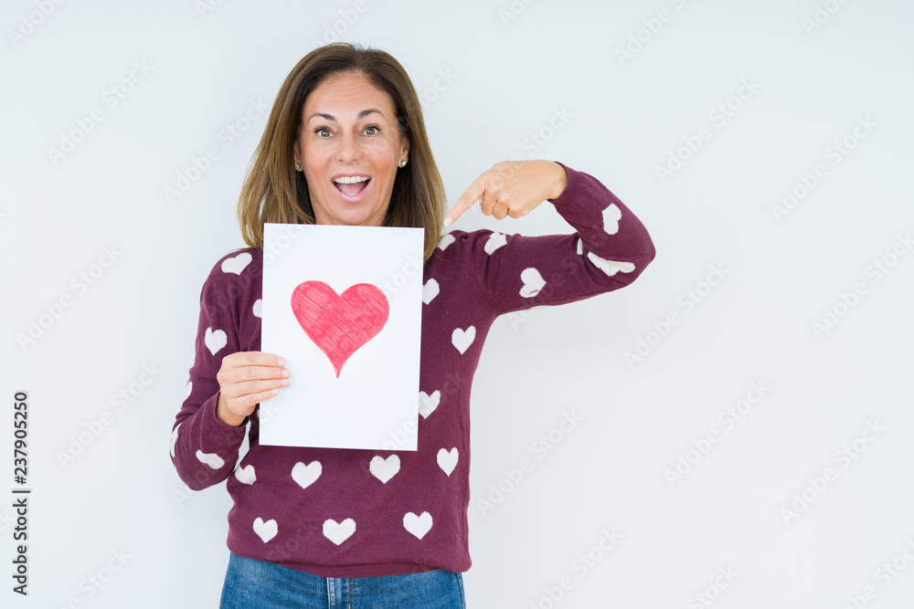 Middle age woman holding card gift with red heart over isolated background very happy pointing with hand and finger Middle age woman holding card gift with red heart over isolated background very happy pointing with hand and finger