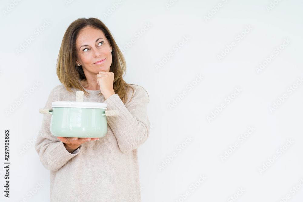 Middle age housewife woman holding iron cooking pot over isolated background serious face thinking about question, very confused idea Middle age housewife woman holding iron cooking pot over isolated background serious face thinking about question, very confused idea