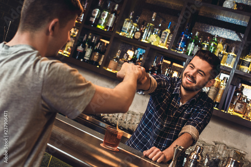 Young bartender standing at bar counter with customer fist bumb cheerful photo