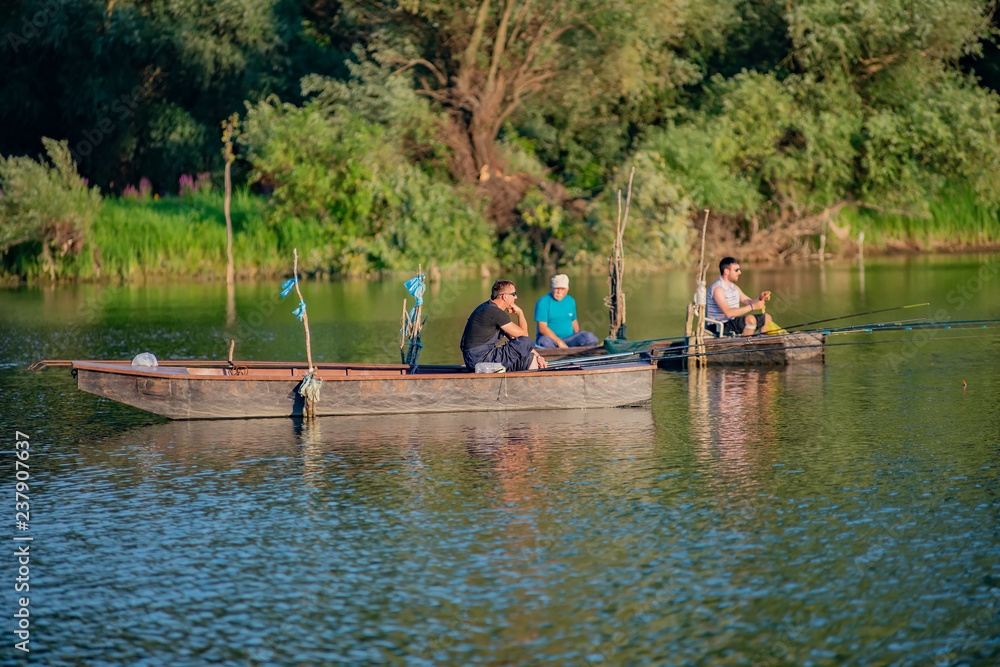 Naklejka premium Novi Sad, Serbia - August 04, 2018: Danube island (Šodroš) near Novi Sad, Serbia. Fishermans sitting in boat and holding fishing rod.