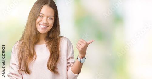 Young beautiful brunette woman wearing pink sweatshirt over isolated background smiling with happy face looking and pointing to the side with thumb up.