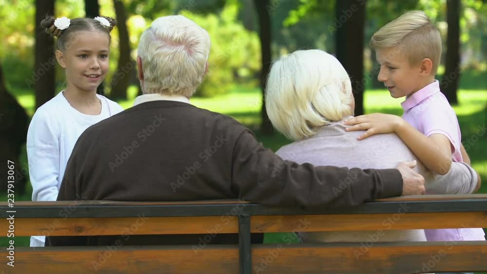 Little cute children happily talking with grandparents sitting on bench in park Little cute children happily talking with grandparents sitting on bench in park