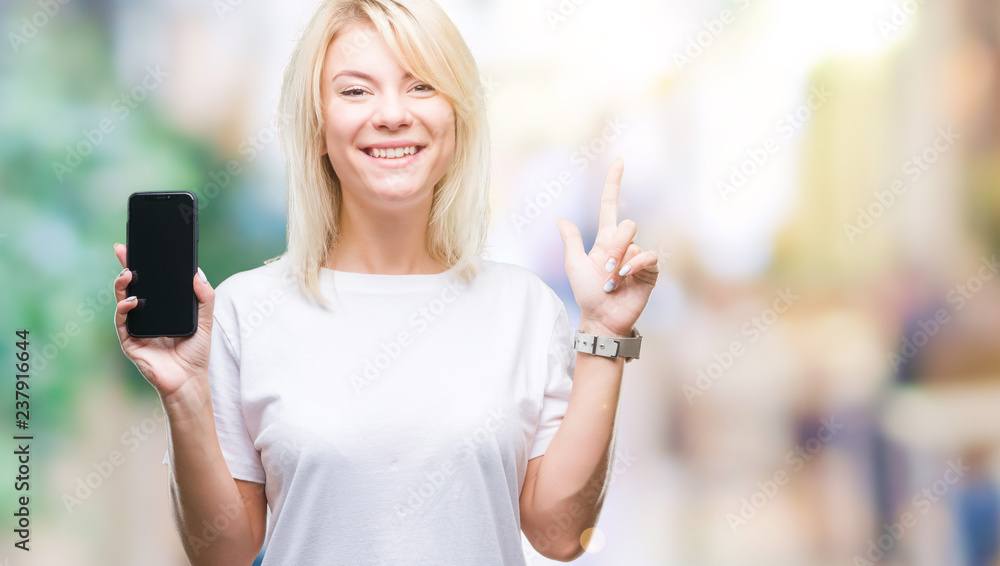 Young beautiful blonde woman showing screen of smartphone over isolated background surprised with an idea or question pointing finger with happy face, number one