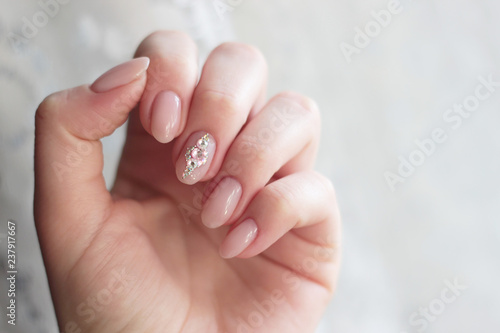 one hand a delicate nude pink manicure with rhinestones on the middle finger close up