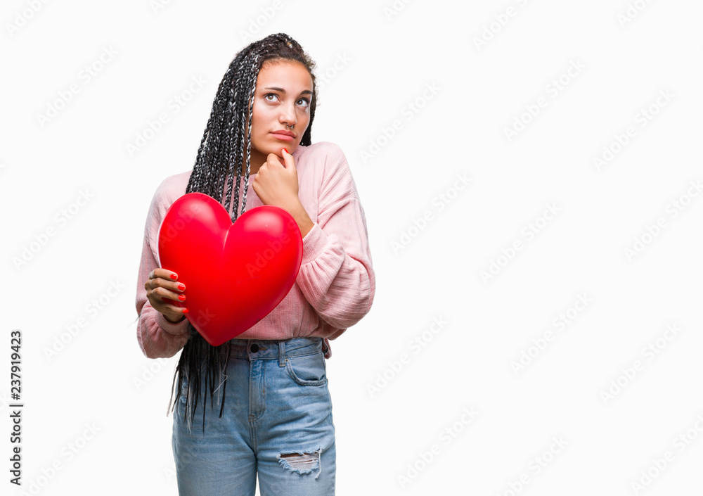 Young braided hair african american girl holding read heart over isolated background serious face thinking about question, very confused idea Young braided hair african american girl holding read heart over isolated background serious face thinking about question, very confused idea