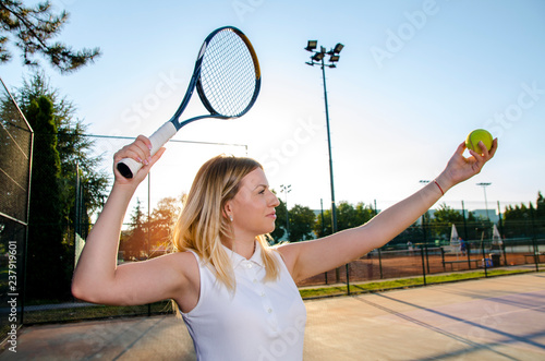 Female tennis player in white dress preparing to serve 