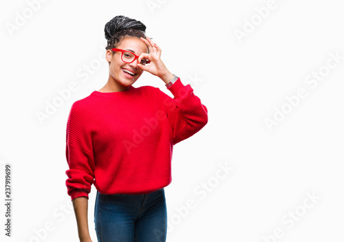 Young braided hair african american girl wearing sweater and glasses over isolated background doing ok gesture with hand smiling, eye looking through fingers with happy face.