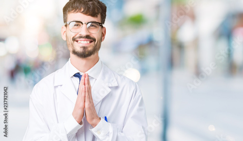 Young professional scientist man wearing white coat over isolated background praying with hands together asking for forgiveness smiling confident.