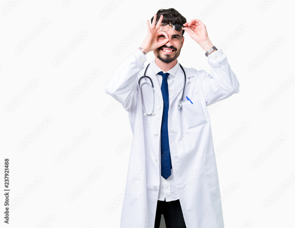 Young doctor man wearing hospital coat over isolated background doing ok gesture with hand smiling, eye looking through fingers with happy face. Young doctor man wearing hospital coat over isolated background doing ok gesture with hand smiling, eye looking through fingers with happy face.