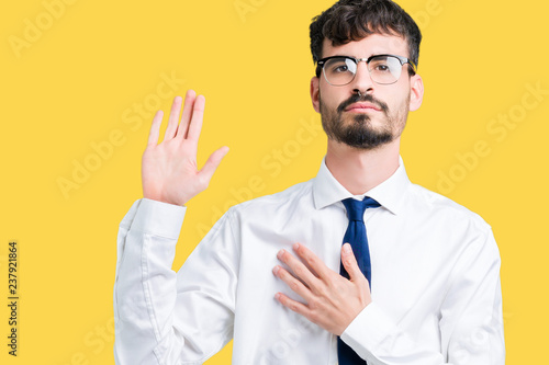 Young handsome business man wearing glasses over isolated background Swearing with hand on chest and open palm, making a loyalty promise oath