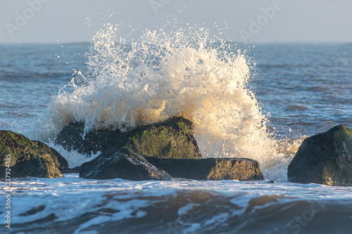 Coastal erosion. Wave crashing against sea flood defence rocks photo