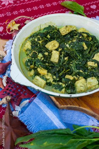 Palak paneer - hot vegetarian traditional Indian food with spinach, cheese, cream gravy, ginger, garlic, garam masala spices. In cast iron skillet pan. Christmas lunch or dinner on red table cloth.