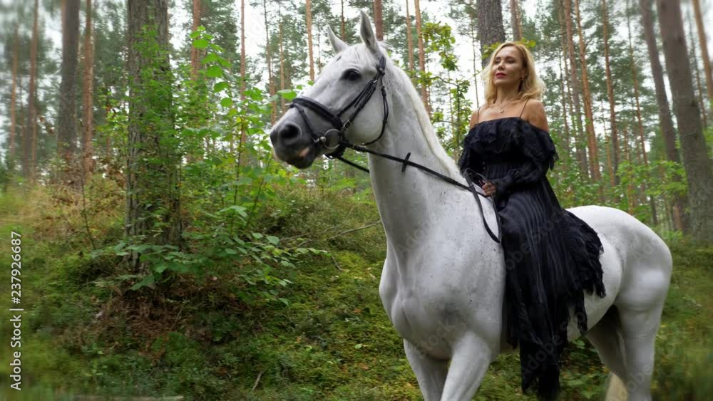 Beautiful woman in evening dress riding a horse in forest Beautiful woman in evening dress riding a horse in forest