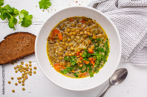 Homemade vegan lentil soup with vegetables, bread and cilantro, white wooden background.