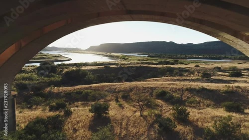 Flying under Arched Bridge to reveal River at Sunrise in Africa