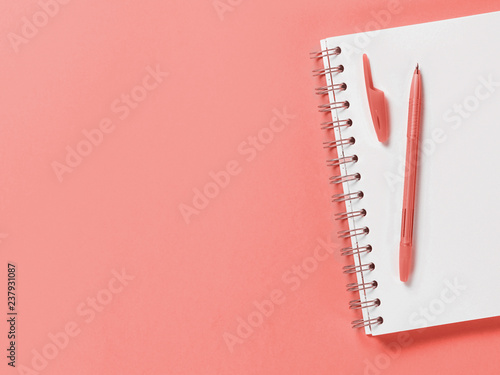 Top view of blank note paper with pen on pliving coral color background. Color of year 2019 Living Coral concept. Top view or flat lay. Copy space for text. Vertical.