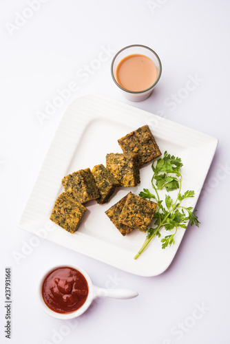 A savory cilantro cake or kothimbir vadi in square shape which is first steamed and then fried until crisp. popular indian snack served with hot tea and tomato ketchup photo