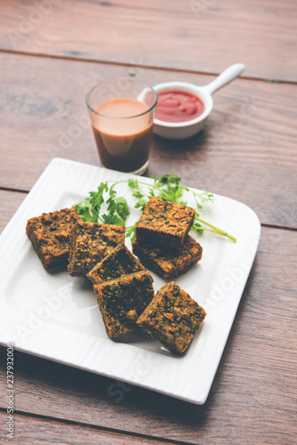 A savory cilantro cake or kothimbir vadi in square shape which is first steamed and then fried until crisp. popular indian snack served with hot tea and tomato ketchup photo