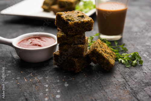 A savory cilantro cake or kothimbir vadi in square shape which is first steamed and then fried until crisp. popular indian snack served with hot tea and tomato ketchup photo