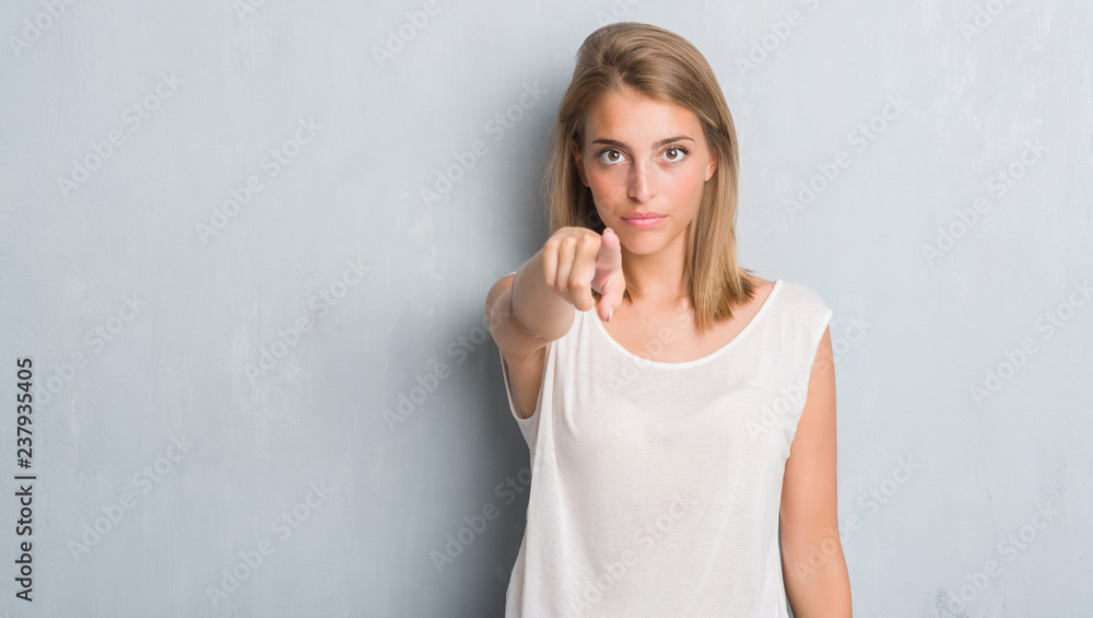 Beautiful young woman standing over grunge grey wall pointing with finger to the camera and to you, hand sign, positive and confident gesture from the front Beautiful young woman standing over grunge grey wall pointing with finger to the camera and to you, hand sign, positive and confident gesture from the front